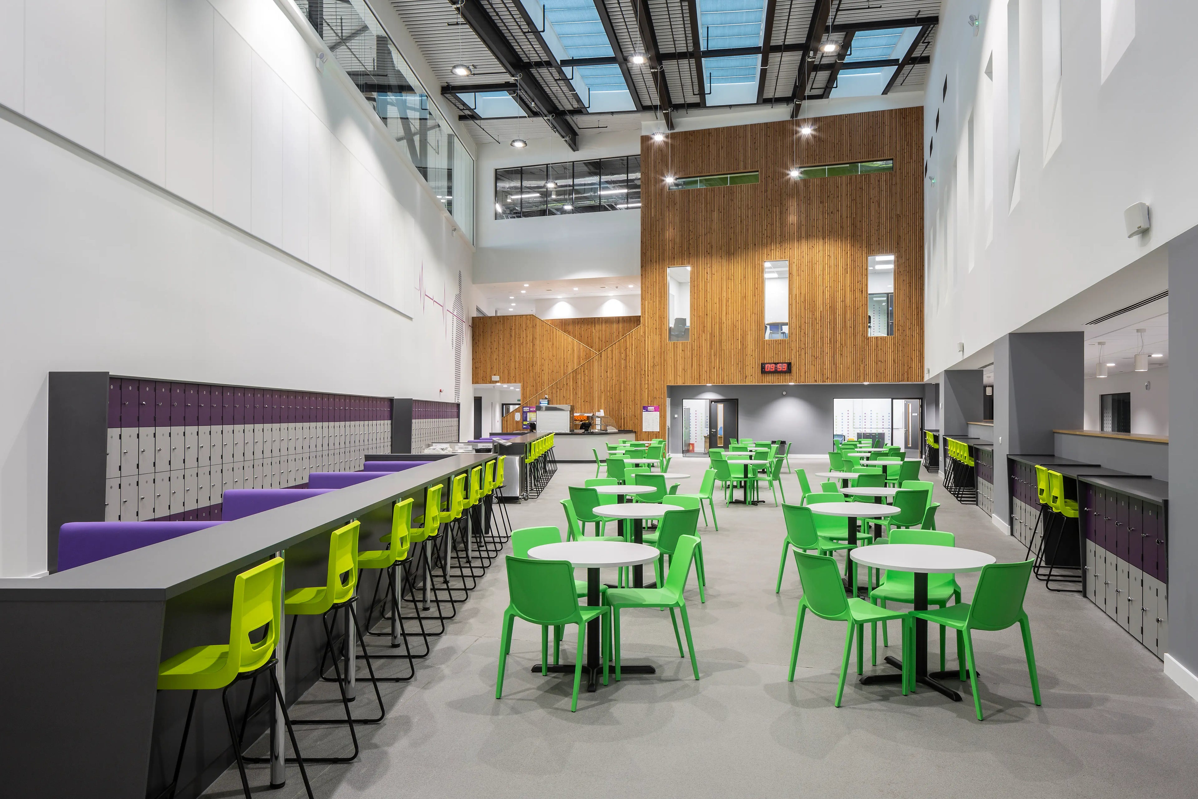 Modern cafeteria with green chairs and tables, lockers, and a kitchen area showcasing the work of a reliable school furniture supplier.