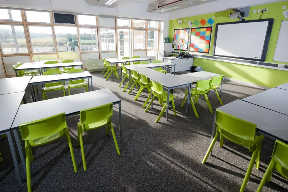 Modern classroom with green chairs and white tables, large windows, and educational posters on the wall. Designed by educational furniture UK supplier Chequered Fox